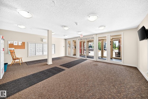 Building entrance with multiple glass-paneled doors, neutral-toned walls, recessed lighting, and textured carpeting - #218 5810 Mullen Pl Nw Nw, Edmonton, AB 