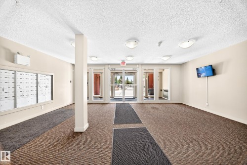 Carpeted entry foyer with integrated floor mats, wall-mounted mailboxes, and multiple ceiling-mounted light fixtures - #218 5810 Mullen Pl Nw Nw, Edmonton, AB 