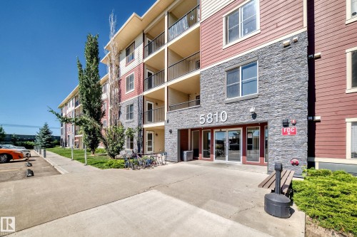Multi-story building featuring stone and siding exterior, private balconies, an exterior entrance, and landscaped grounds - #218 5810 Mullen Pl Nw Nw, Edmonton, AB 