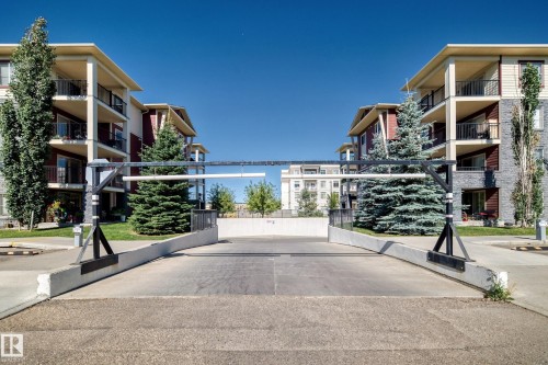 Exterior featuring multiple balconies, stone veneer accents, and an underground parking entrance with gate - #218 5810 Mullen Pl Nw Nw, Edmonton, AB 