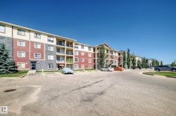 Multi-story building featuring balconies, red and grey siding, and ample surface parking - 