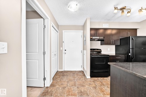 Kitchen featuring dark wood-finish cabinetry, black appliances, and a built-in oven - #218 5810 Mullen Pl Nw Nw, Edmonton, AB 