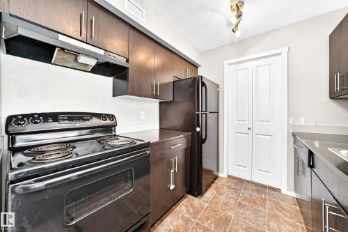 Full-size black appliances, wood-finish cabinetry, stone-look countertops, and tiled flooring - #218 5810 Mullen Pl Nw Nw, Edmonton, AB 