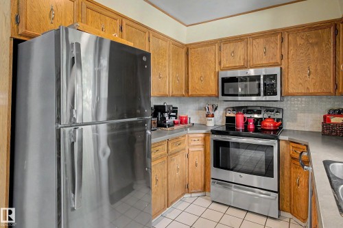 Kitchen featuring wood cabinetry, stainless steel appliances, and a tiled backsplash - 36 Lodgepole Crescent, St. Albert, AB 