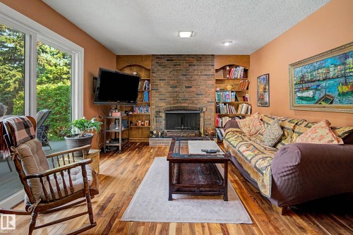 Wood-finish flooring, brick fireplace with a hearth, built-in shelving, and large sliding glass doors leading to an exterior deck - 36 Lodgepole Crescent, St. Albert, AB 