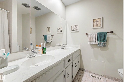 Dual vanity with integrated sinks, expansive wall-mounted mirror, white shaker-style cabinetry, and tiled flooring - 36 Lodgepole Crescent, St. Albert, AB 