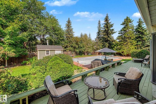 Expansive outdoor deck with a private backyard, featuring a swimming pool, mature trees, and a storage shed - 36 Lodgepole Crescent, St. Albert, AB 