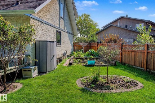 Manicured lawn with a circular brick-edged planter, fenced garden beds, and a wood lattice fence - 36 Lodgepole Crescent, St. Albert, AB 