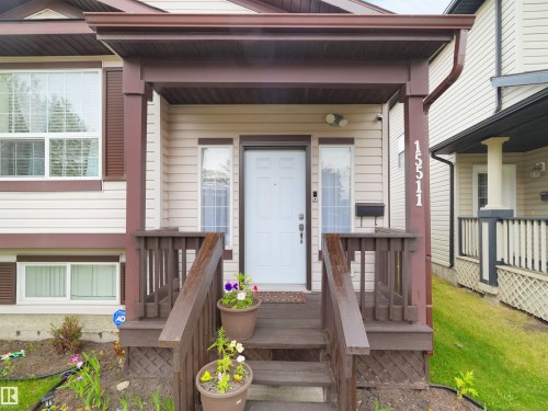 Covered front porch with wood railings and steps, featuring exterior sconce lighting and a white entry door - 15511 45 Street Nw, Edmonton, AB 