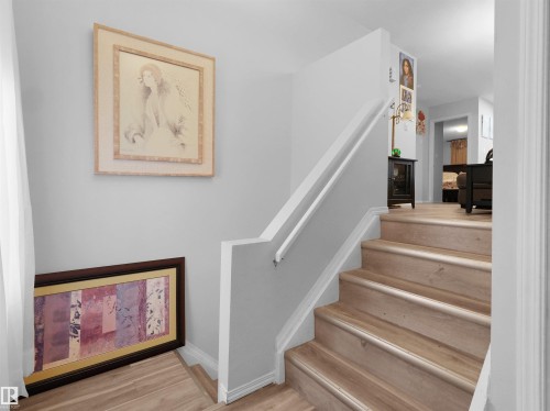 Staircase with wood-finish treads and risers, featuring a white handrail and a painted wall finish - 15511 45 Street Nw, Edmonton, AB 