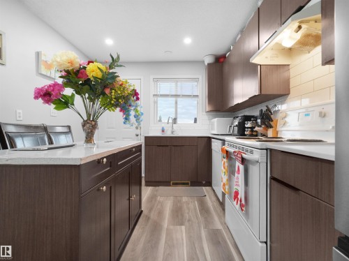 Kitchen with wood-finish flooring, wood-look cabinetry, light countertops, and white subway tile backsplash - 15511 45 Street Nw, Edmonton, AB 