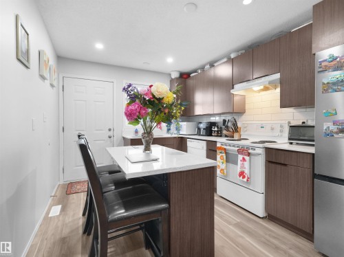 Kitchen featuring wood-finish cabinetry, white countertops, subway tile backsplash, and light wood-finish flooring - 15511 45 Street Nw, Edmonton, AB 