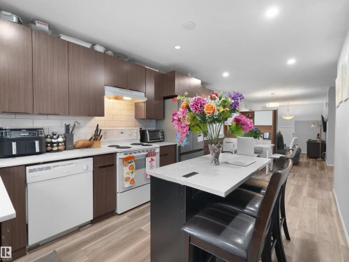 Open-concept kitchen with wood-finish flooring, white subway tile backsplash, recessed lighting, and a kitchen island with seating - 15511 45 Street Nw, Edmonton, AB 