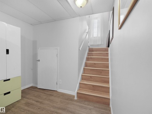 Wood-finish flooring, staircase with wood treads, white wall finishes, and a flush mount ceiling light fixture - 15511 45 Street Nw, Edmonton, AB 