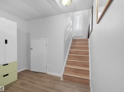 Wood-finish flooring, staircase with wood treads, white wall finishes, and a flush mount ceiling light fixture - 
