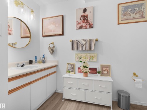 White vanity with integrated sink, gold-finish circular mirror, gold-finish three-light fixture, and wood-finish flooring - 15511 45 Street Nw, Edmonton, AB 