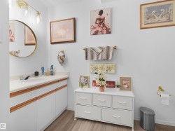 White vanity with integrated sink, gold-finish circular mirror, gold-finish three-light fixture, and wood-finish flooring - 