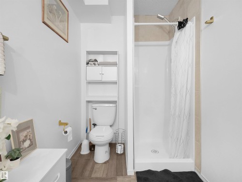 Three-piece bathroom featuring a shower stall, toilet, and wood-finish flooring - 15511 45 Street Nw, Edmonton, AB 