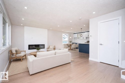 Open-concept living space featuring wood-finish flooring, a linear fireplace with a textured white surround, recessed lighting, and large windows AI VIRTUAL STAGING - 904 Knottwood S Nw, Edmonton, AB 