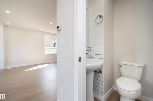Pedestal sink with subway tile backsplash, toilet, and wood-finish flooring - 904 Knottwood S Nw, Edmonton, AB 