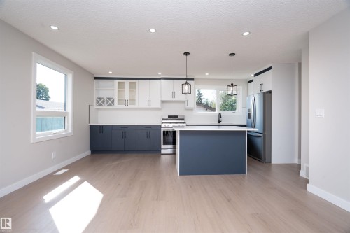 Open-concept kitchen featuring two-tone cabinetry, stainless steel appliances, a center island, recessed lighting, and wood-finish flooring - 904 Knottwood S Nw, Edmonton, AB 