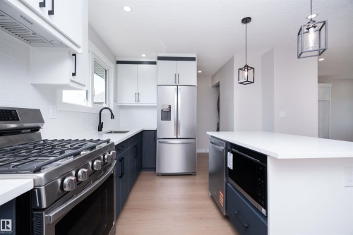 Kitchen featuring stainless steel appliances, white quartz countertops, two-tone cabinetry, wood-finish flooring, and pendant lighting - 904 Knottwood S Nw, Edmonton, AB 
