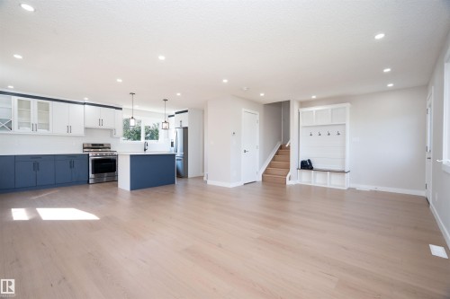 Open-concept living area featuring light wood-finish flooring, a contemporary kitchen with two-tone cabinetry and stainless-steel appliances, a kitchen island with pendant lighting, and a built-in bench with storage - 904 Knottwood S Nw, Edmonton, AB 