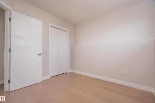 Pale wood-finish flooring with white baseboards, a white interior door with brushed nickel hardware, and a white bi-fold closet door - 904 Knottwood S Nw, Edmonton, AB 