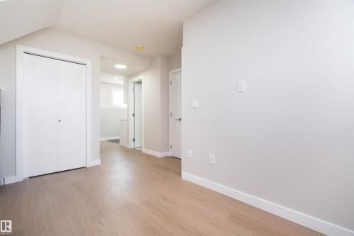 Light wood-finish flooring, white bi-fold closet doors, white interior doors, and a round overhead light fixture - 904 Knottwood S Nw, Edmonton, AB 