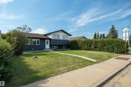 Split-level exterior with dark siding and white trim accents, featuring a well-maintained lawn, mature perimeter landscaping, and a concrete pathway - 904 Knottwood S Nw, Edmonton, AB 
