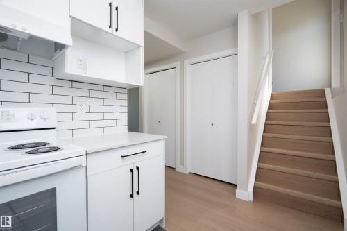 White kitchen cabinetry with matte black hardware, white subway tile backsplash, white countertop, and wood-finish flooring - 904 Knottwood S Nw, Edmonton, AB 