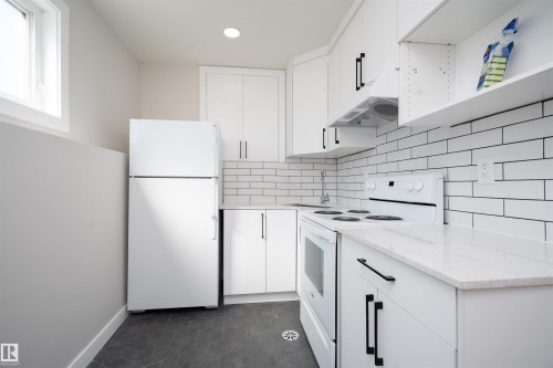 Kitchen featuring white cabinetry, white subway tile backsplash, white appliances, light-colored countertops, and dark hexagonal floor tiles - 904 Knottwood S Nw, Edmonton, AB 