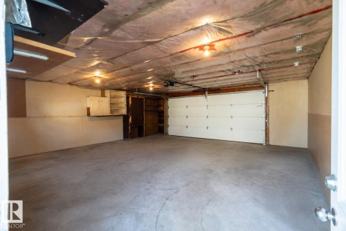 Attached garage with a roll-up door, exposed ceiling insulation, built-in shelving, and a concrete floor - 904 Knottwood S Nw, Edmonton, AB 