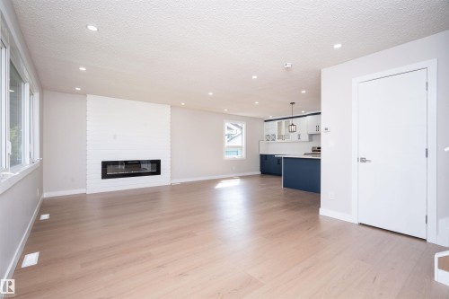 Expansive open-concept living area featuring wood-finish flooring, a linear electric fireplace with a white brick surround, recessed lighting, and large windows - 904 Knottwood S Nw, Edmonton, AB 