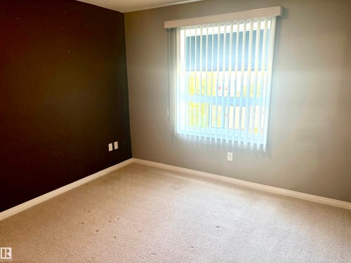 Carpeted room featuring a large window with vertical blinds, contrasting wall colors, and white trim - #1304 9363 Simpson Dr Nw, Edmonton, AB 