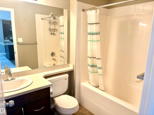 Bathroom featuring a built-in vanity with a white basin sink, dark wood-finish cabinetry, and an integrated bathtub with a shower - #1304 9363 Simpson Dr Nw, Edmonton, AB 