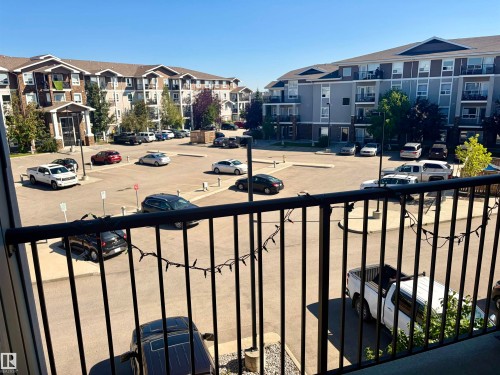 Open-air balcony with black metal railings overlooking a paved parking area and multi-story residential buildings featuring exterior balconies - #1304 9363 Simpson Dr Nw, Edmonton, AB 
