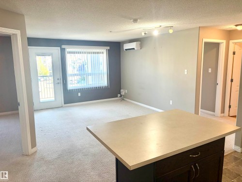 Light-colored carpeting throughout, featuring an attached balcony with metal railing, an installed wall-mounted AC unit, and a track lighting fixture - #1304 9363 Simpson Dr Nw, Edmonton, AB 