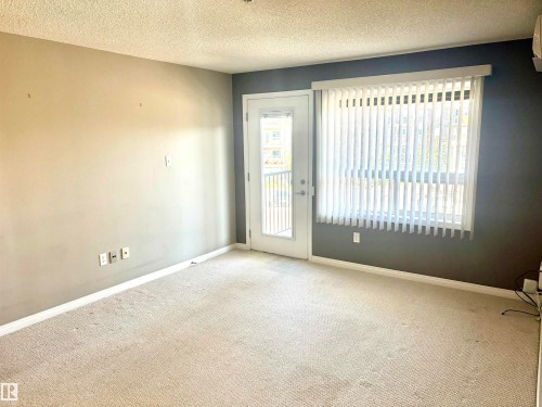 Wall-to-wall carpeting, neutral wall colors, a full-light door, and an oversized window with vertical blinds - #1304 9363 Simpson Dr Nw, Edmonton, AB 