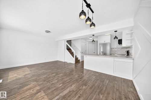Open-concept living space featuring wood-finish flooring, a contemporary kitchen island with white cabinetry, stainless steel appliances, and a staircase with glass panel railing - 13005 162A Avenue Nw, Edmonton, AB - Indoor