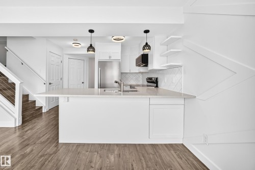 Open-concept kitchen featuring an eat-at island with a light-toned countertop, white cabinetry, stainless steel appliances, and a diagonal tile backsplash - 13005 162A Avenue Nw, Edmonton, AB - Indoor Photo Showing Kitchen