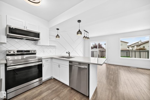 Modern kitchen featuring white shaker cabinetry, stainless steel appliances, a tile backsplash, and light-toned countertops - 13005 162A Avenue Nw, Edmonton, AB - Indoor Photo Showing Kitchen With Stainless Steel Kitchen With Double Sink