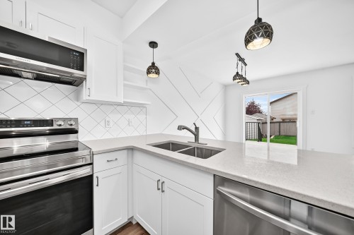 Contemporary kitchen featuring white cabinetry, stainless steel appliances, light-toned countertops, a tile backsplash with a diagonal pattern, and a double basin sink with a single-handle faucet - 13005 162A Avenue Nw, Edmonton, AB - Indoor Photo Showing Kitchen With Stainless Steel Kitchen With Double Sink With Upgraded Kitchen