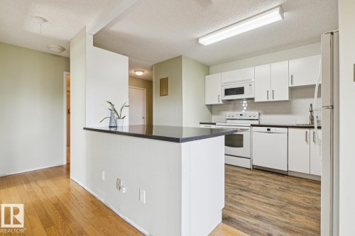 Kitchen featuring white cabinetry, dark countertops, white appliances, and a tile backsplash - #905 9929 113 St Nw, Edmonton, AB 