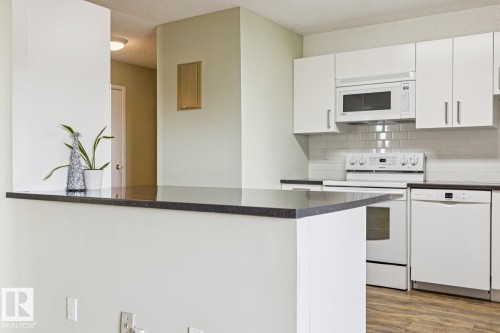 Kitchen featuring white cabinetry, subway tile backsplash, dark countertops, and wood-finish flooring - #905 9929 113 St Nw, Edmonton, AB 