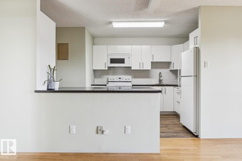White cabinetry, stainless steel sink, black countertops, white subway tile backsplash, and wood-finish flooring - #905 9929 113 St Nw, Edmonton, AB 