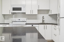 White cabinetry, dark stone countertops, white subway tile backsplash, stainless steel sink with gooseneck faucet, and white appliances - 