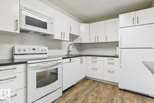 Kitchen featuring white cabinetry, dark countertops, white subway tile backsplash, stainless steel sink with a gooseneck faucet, and wood-finish flooring - #905 9929 113 St Nw, Edmonton, AB 