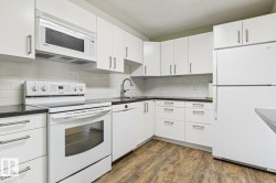 Kitchen featuring white cabinetry, dark countertops, white subway tile backsplash, stainless steel sink with a gooseneck faucet, and wood-finish flooring - 