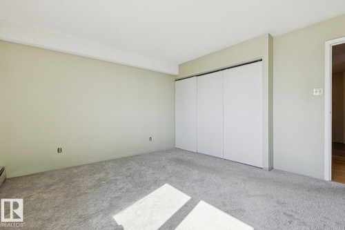Carpeted room featuring a white ceiling, light-toned walls, and a multi-panel closet with white doors - #905 9929 113 St Nw, Edmonton, AB 